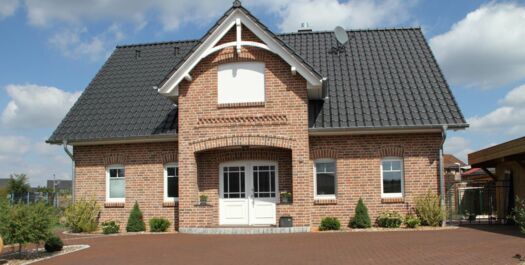 Einfamilienhaus aus Klinker mit vorgesetztem dritten Giebel, dunkle Dachpfannen, weiße Fenster und Türen